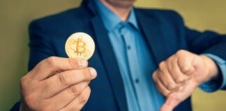 Biznesmen trzyma Bitcoina i wskazuje kciukiem w dół