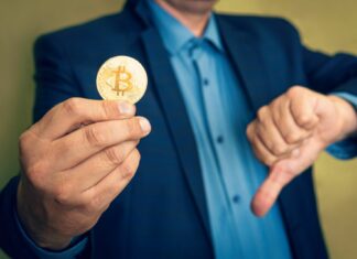 Biznesmen trzyma Bitcoina i wskazuje kciukiem w dół